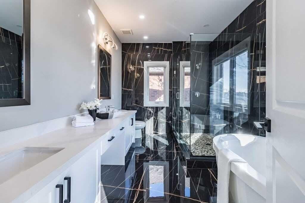 An ensuite tiled floor to ceiling in black marble-effect porcelain, with a glass shower panel and a white vanity with black handles