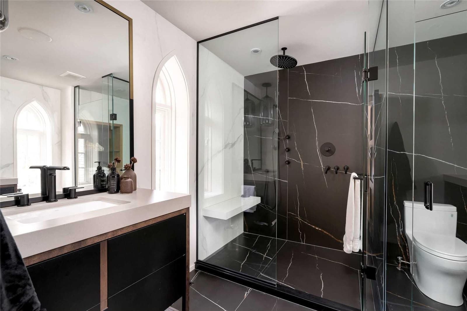 An ensuite with a black marble-effect slab shower behind frameless glass, a white quartz vanity and tall windows