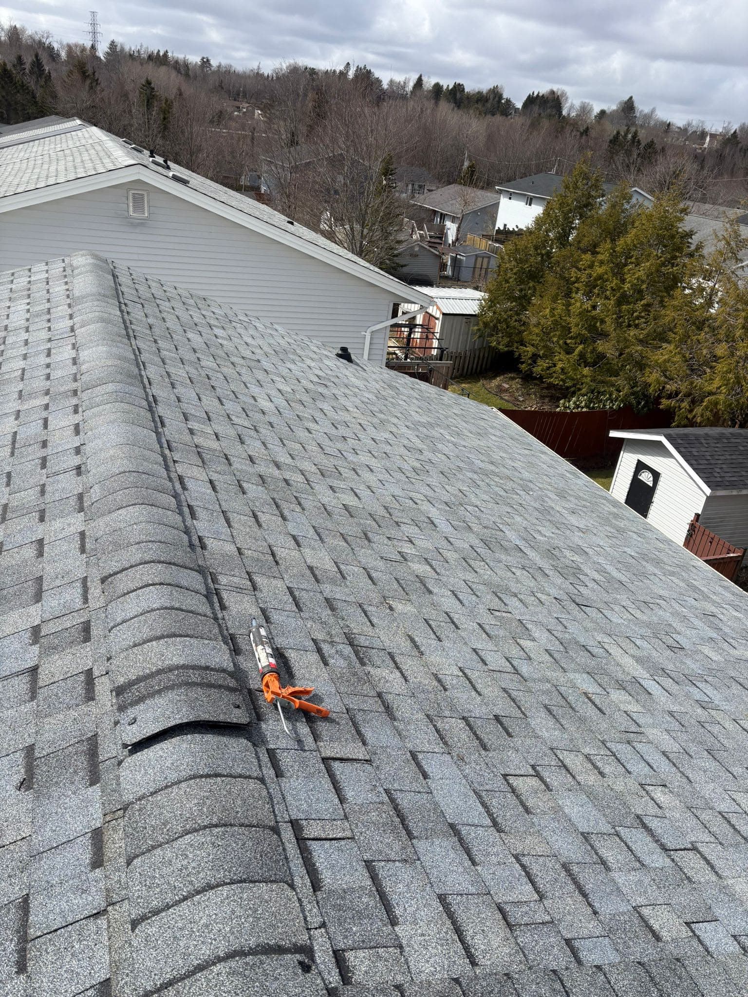 A completed hip roof in grey architectural shingles with ridge cap, over a street of gable-roofed houses